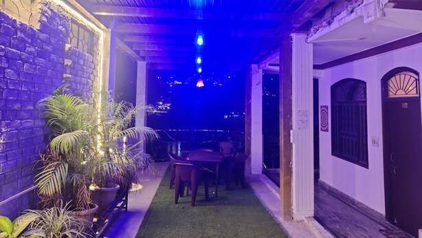 An indoor corridor with a brick wall, potted plants, a wooden table, and chairs. - Shri Ganga View Guest House (Rishikesh)