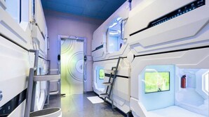 Een futuristisch hotelkamer met een centraal bedieningspaneel, een zithoek met een scherm, en een kleine tafel.