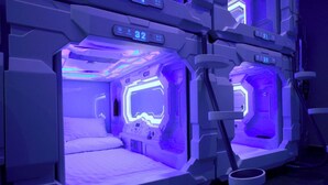 Een futuristische kamer met een bed en bedieningspanelen, voorzien van digitale displays en blauw sfeerverlichting.