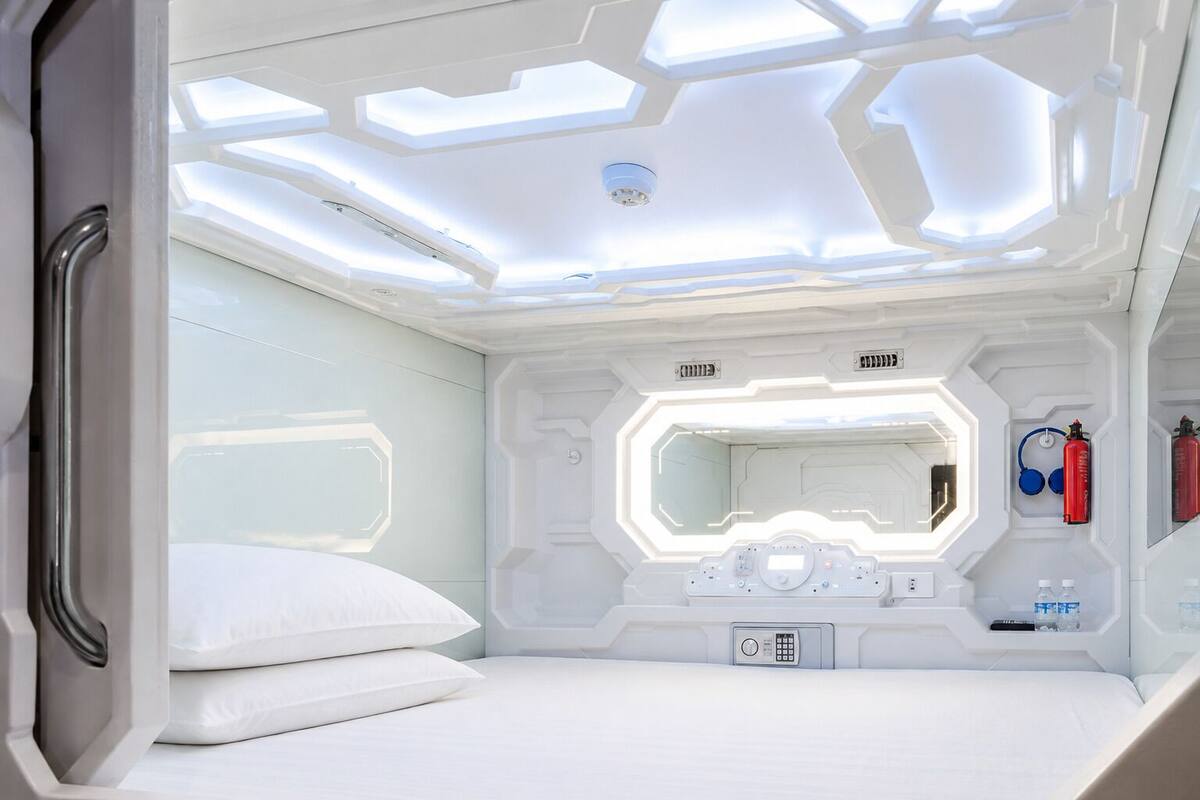 Quarto futurista com beliche, painel de controle, espelho e equipamentos de emergência.