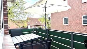 Une terrasse extérieure avec une table et des chaises, un parasol blanc et un bâtiment en briques en arrière-plan.
