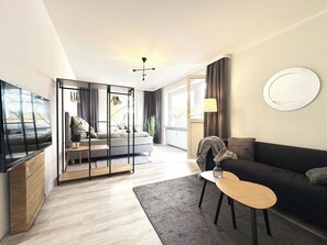 Een moderne woonkamer met een bank, een salontafel, een televisie en een bed met uitzicht op het groen.