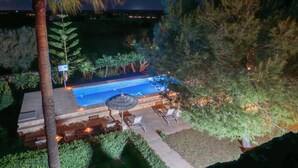 An outdoor swimming pool with a sunken seating area and a small table, surrounded by various plants and trees. - Finca near Es Trenc Beach (Campos)
