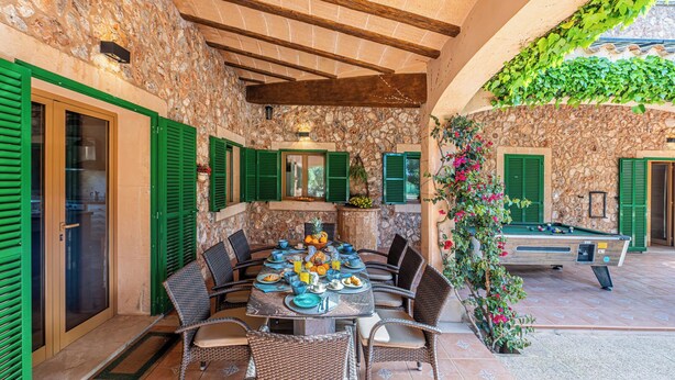 A stone-walled outdoor dining area with green shutters, wicker furniture, and a pool table. - Finca near Es Trenc Beach (Campos)