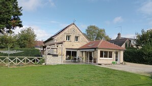 A two-story stone house with a sloped roof, a covered patio, and a fenced yard. - Bed and breakfast in the heart of nature (basic room rate) (Saint-Roch)
