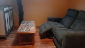 A room with a sloped ceiling, a wooden table with a grid pattern, a grey sofa, and a cabinet with glass doors. - Bed and breakfast in the heart of nature (basic room rate) (Saint-Roch)