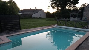 A rectangular swimming pool with a tiled edge, surrounded by a grassy area and a stone wall. - Bed and breakfast in the heart of nature (basic room rate) (Saint-Roch)