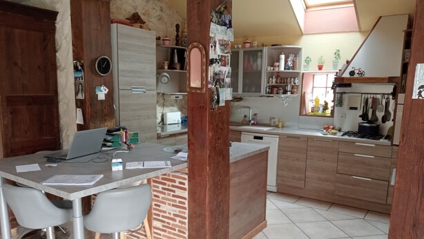 A compact kitchen with a dining area, wooden cabinets, a built-in refrigerator, and a small island with stools. - Bed and breakfast in the heart of nature (basic room rate) (Saint-Roch)