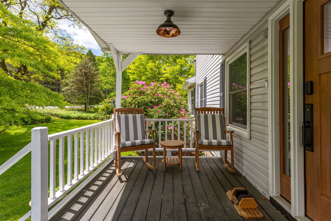 Een houten veranda met twee gestreepte stoelen en een kleine ronde tafel, omringd door een witte balustrade.