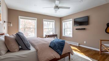 A bedroom with a bed, a ceiling fan, a TV, and large windows.