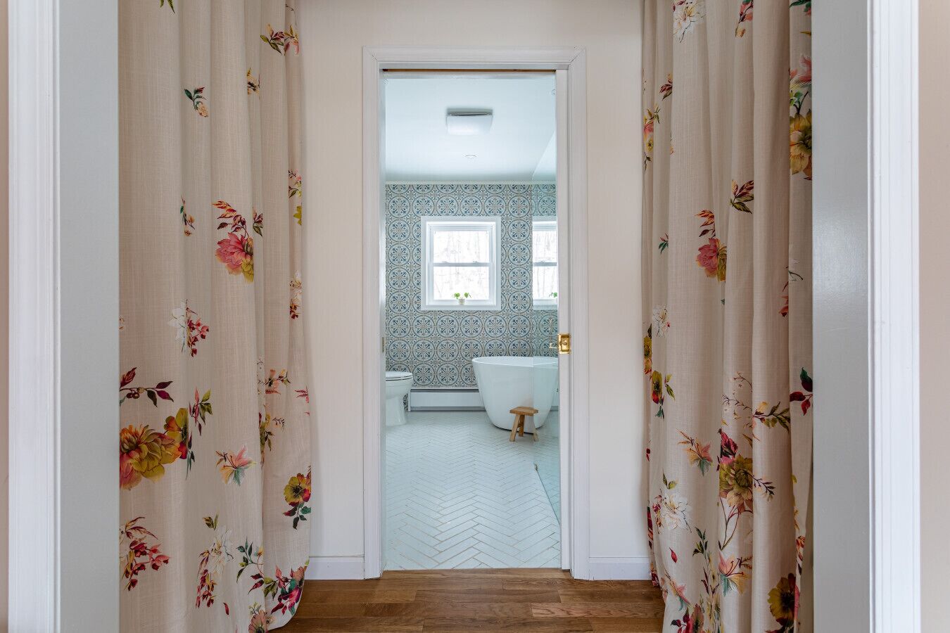 A bathroom with a herringbone floor, a freestanding bathtub, and a small stool.
