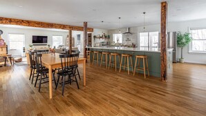 Uma cozinha ampla com piso de madeira, uma sala de jantar com mesa e cadeiras, e um balcão com banquetas.