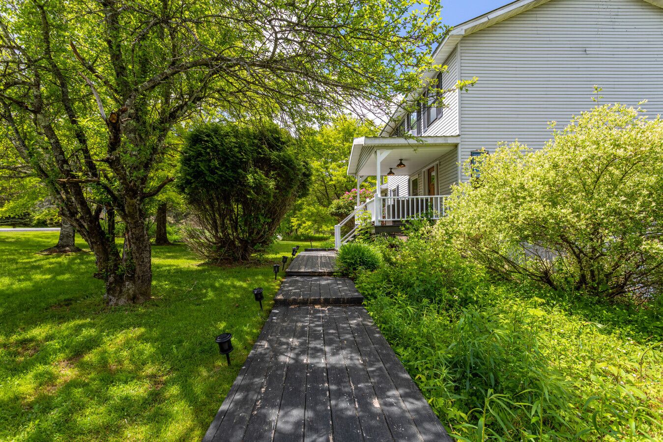 A wooden pathway leading to a white house with a porch and a covered entryway.