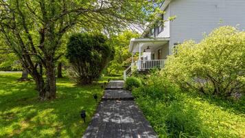 A wooden pathway leading to a white house with a porch and a covered entryway.