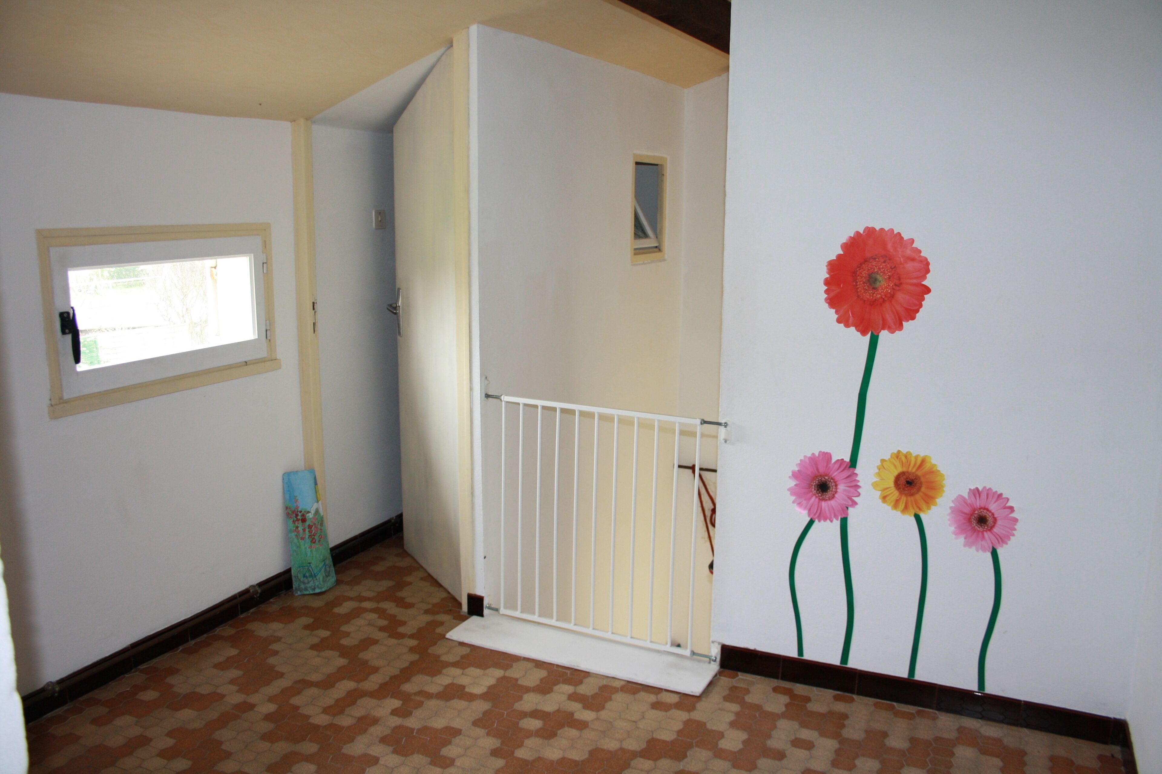 Um corredor com uma porta branca, uma pequena janela e uma parede com uma pintura floral.