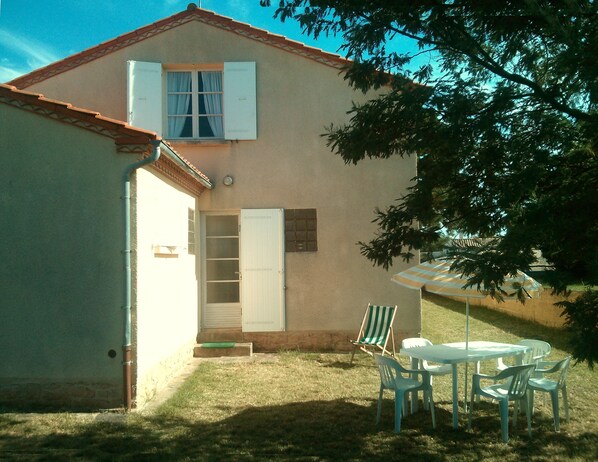 Una casa con un pequeño patio, una puerta blanca y una ventana con persianas.