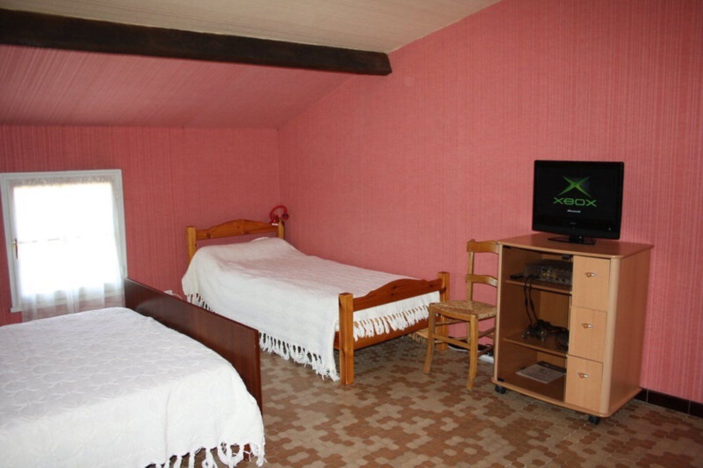 Une chambre avec deux lits, une commode en bois et un téléviseur posé sur un meuble.