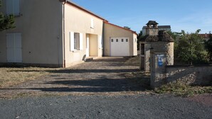 Un edificio con tetto in tegole rosse, struttura in pietra con insegna blu, e vialetto sterrato che conduce a un portone garage bianco.