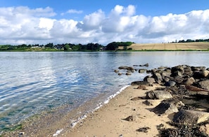 A clear lake with a rocky shoreline, calm water, and a distant view of houses and trees.