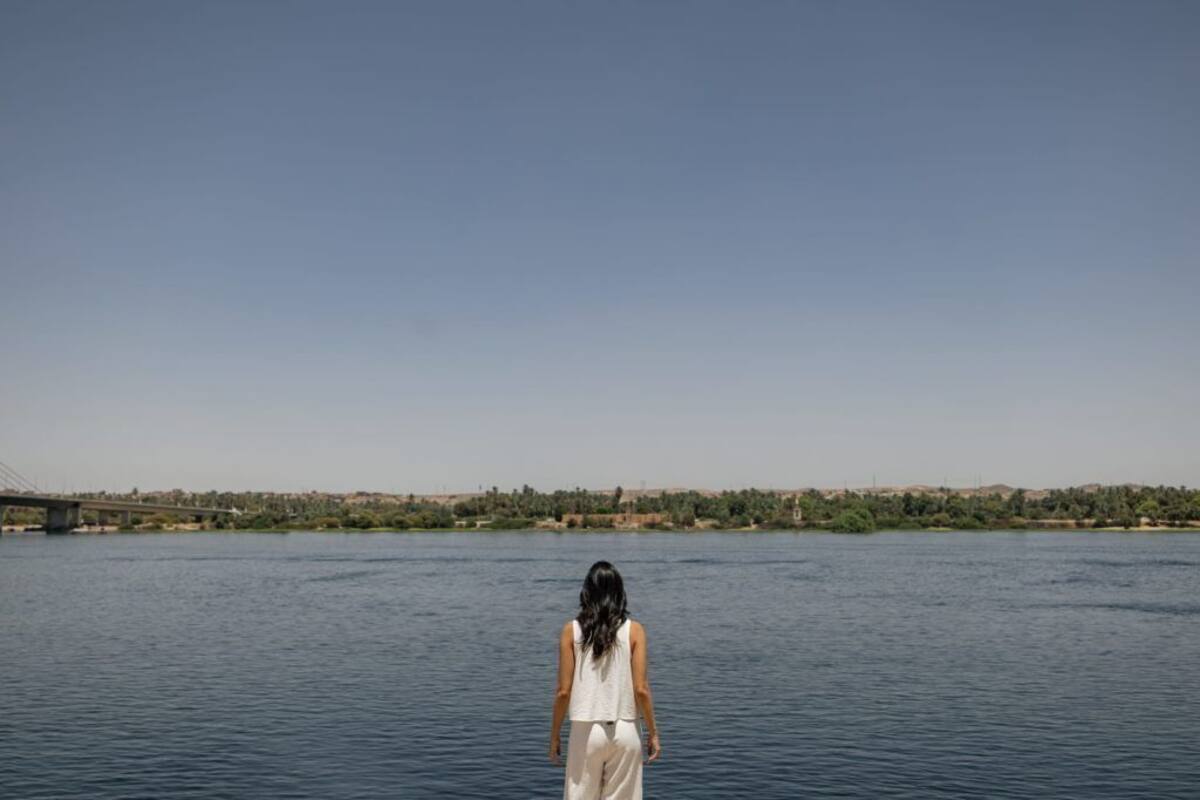 A person standing by a body of water with a bridge in the background.