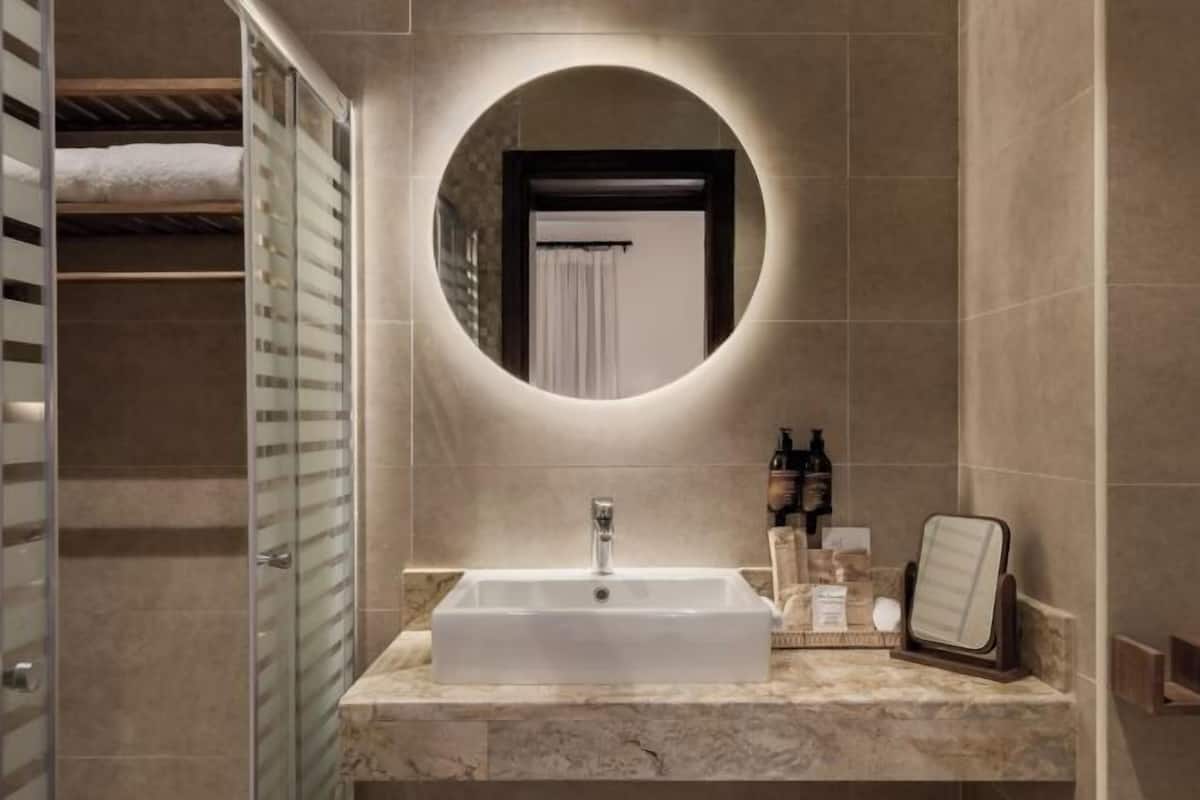 Un baño moderno con un lavamanos grande y rectangular, un espejo redondo y un box de ducha de vidrio.