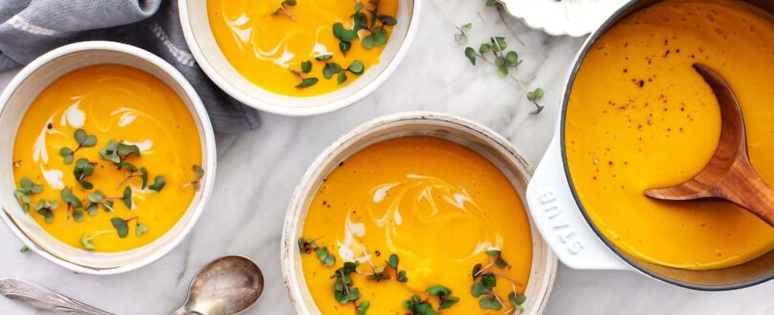 Three bowls of creamy soup garnished with microgreens, a spoon, and a pot.