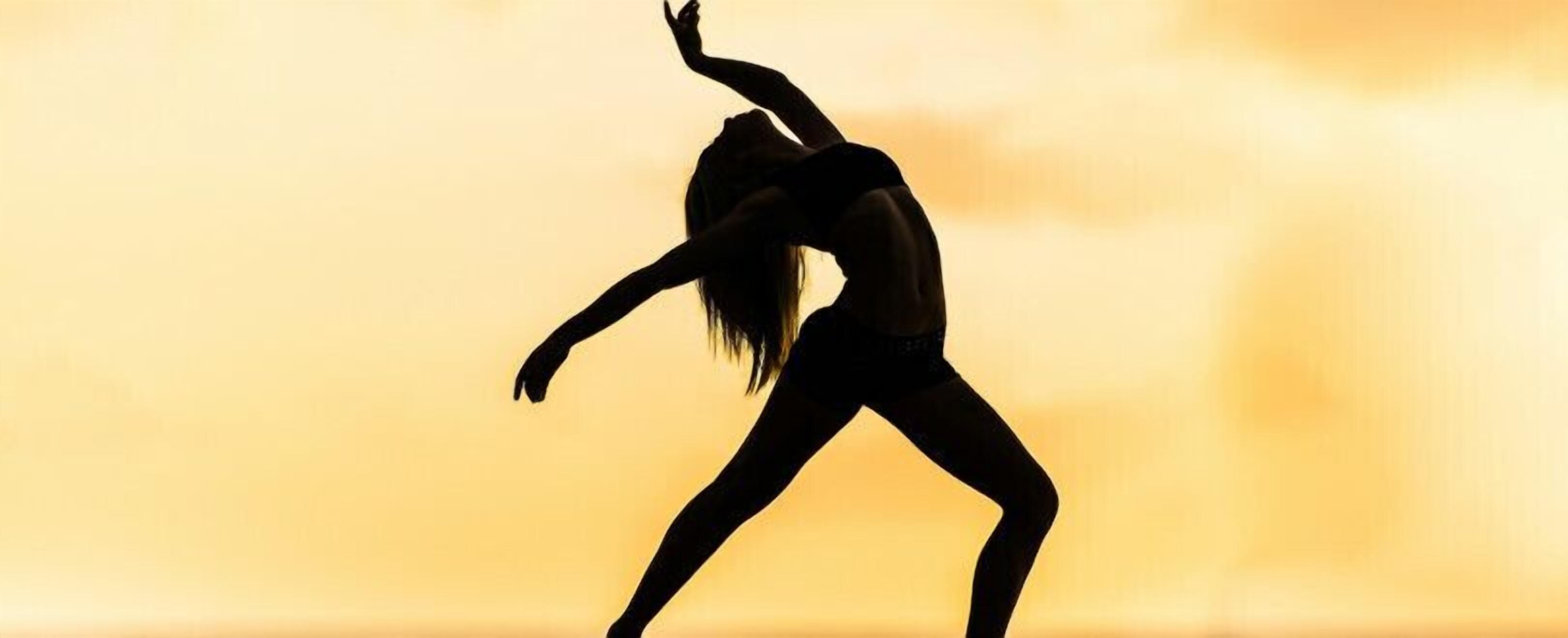 A silhouette of a person performing a dance against a sunset backdrop.