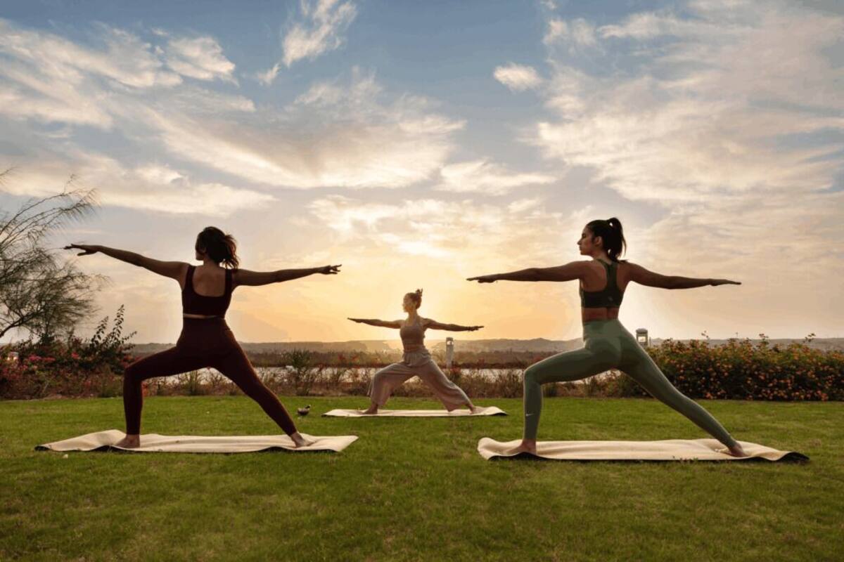 Three individuals practicing yoga outdoors on mats.