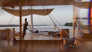 A wooden deck with a hammock, a person standing, and a view of the water. - MGM Wellness Clinic (Aswan)