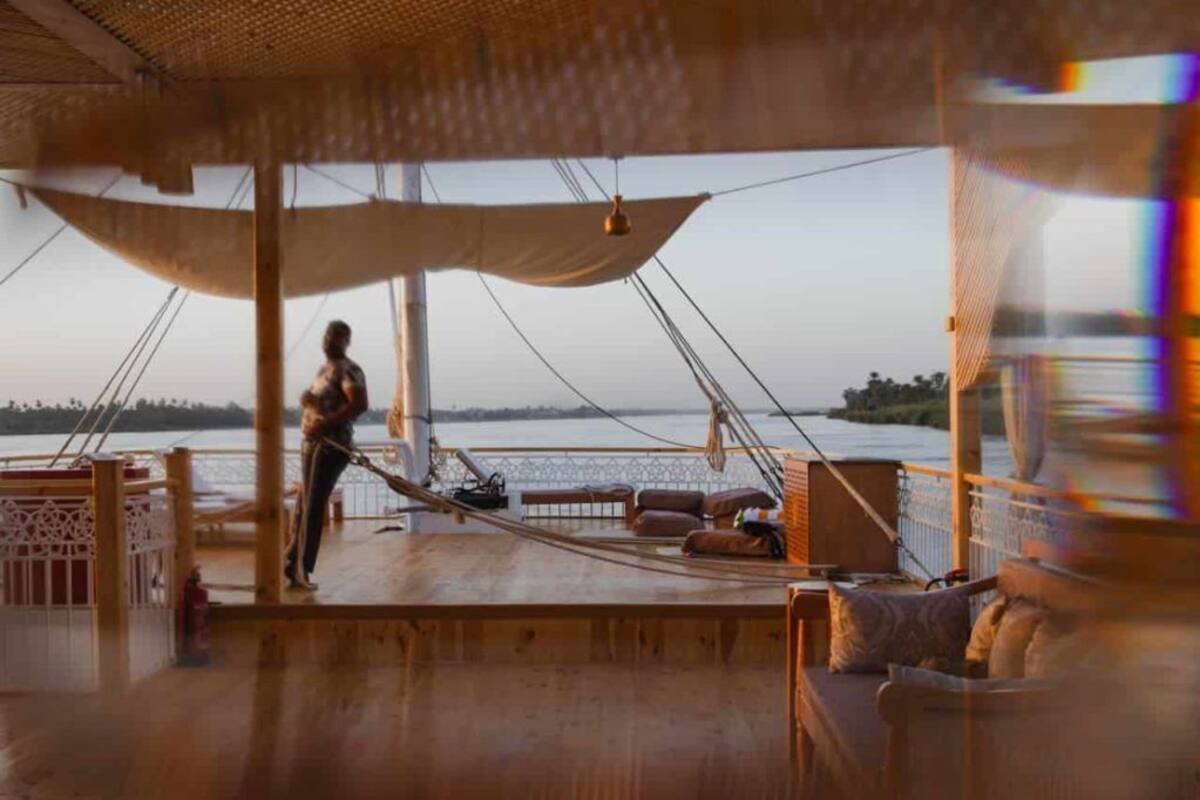 A wooden deck with a hammock, a person standing, and a view of the water.