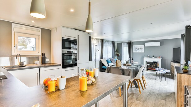 Une cuisine moderne dotée d’un four encastré, un coin repas avec une table et des chaises, et un espace de vie agrémenté d’une cheminée.