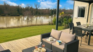 Une terrasse avec des meubles d’extérieur, une table à manger et une vue sur un lac.