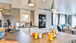 Une cuisine moderne équipée d’un four encastré, d’une machine à café et d’un coin repas avec une table mise pour le petit-déjeuner.