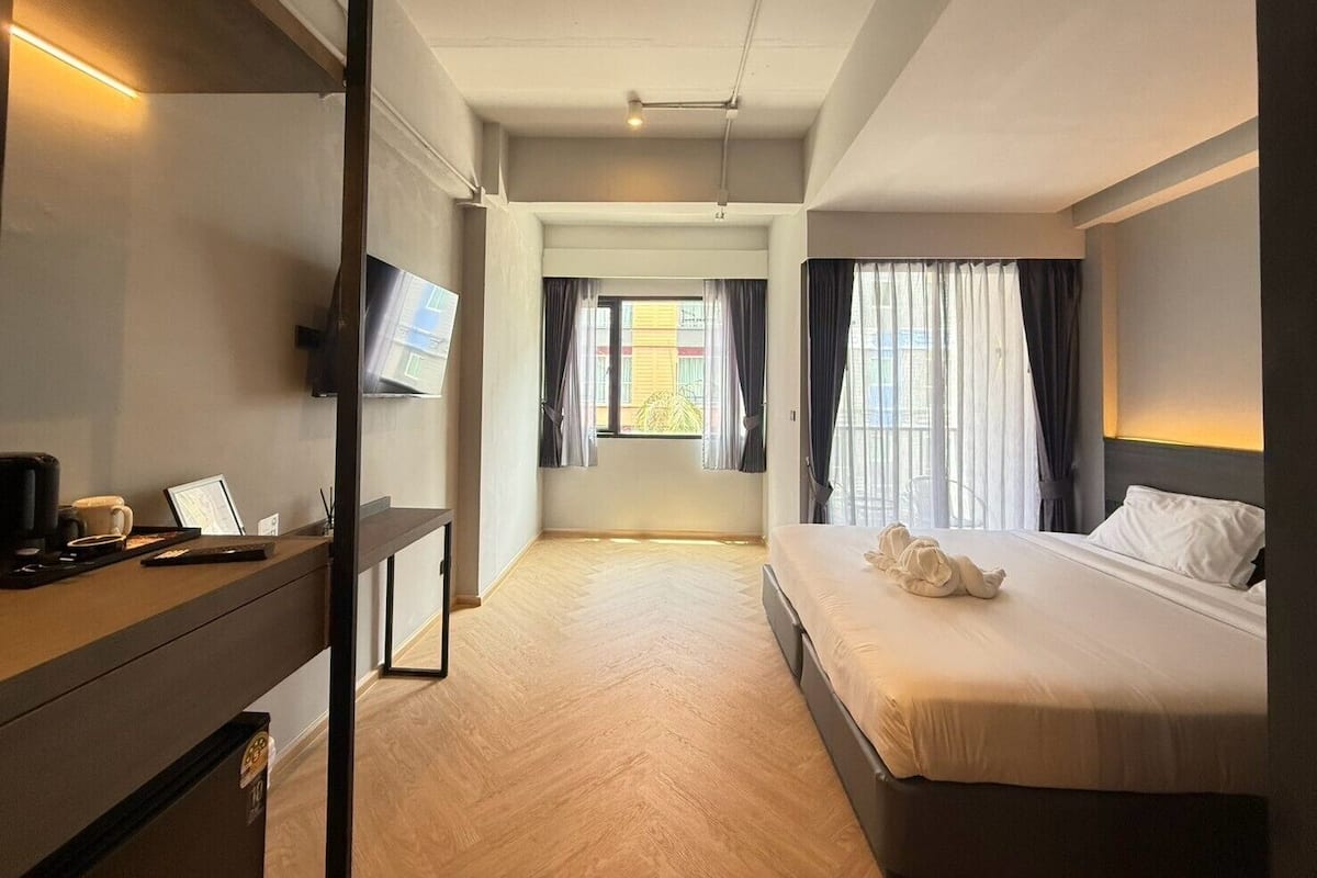 A hotel room with a bed, a desk with a computer, a TV, and a window with curtains.