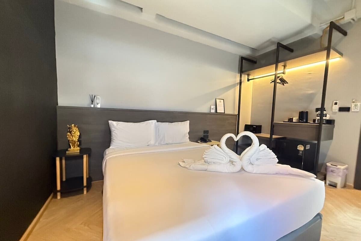 A modern hotel room with a large bed, a bedside table with a lamp, a mirror, and a small statue.