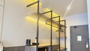 A modern hotel room with a wooden desk, a black hanging rack, and a grey door with a fire escape plan sign. - Leon's Loft House (Patong)