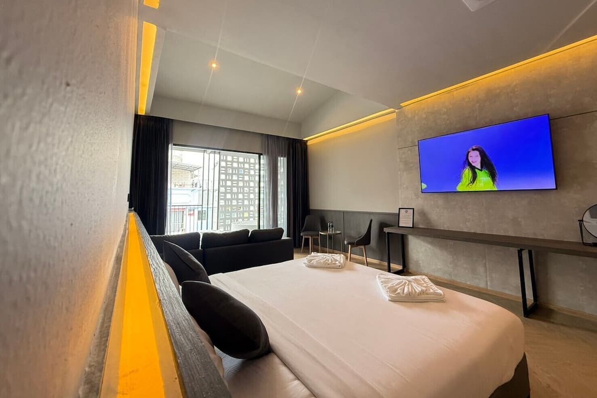 A modern hotel room with a large bed, a flat-screen TV mounted on the wall, and a balcony with a view of the city.