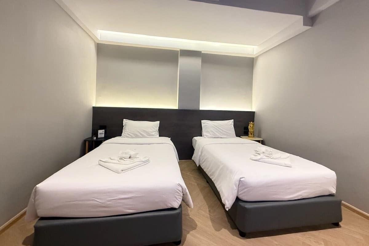 A modern hotel room with two beds, a skylight, and a nightstand with a lamp.