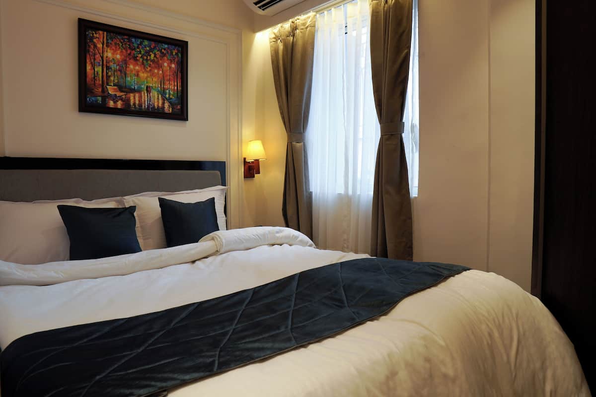 A neatly made bed with a dark headboard, a painting on the wall, and a window with curtains.