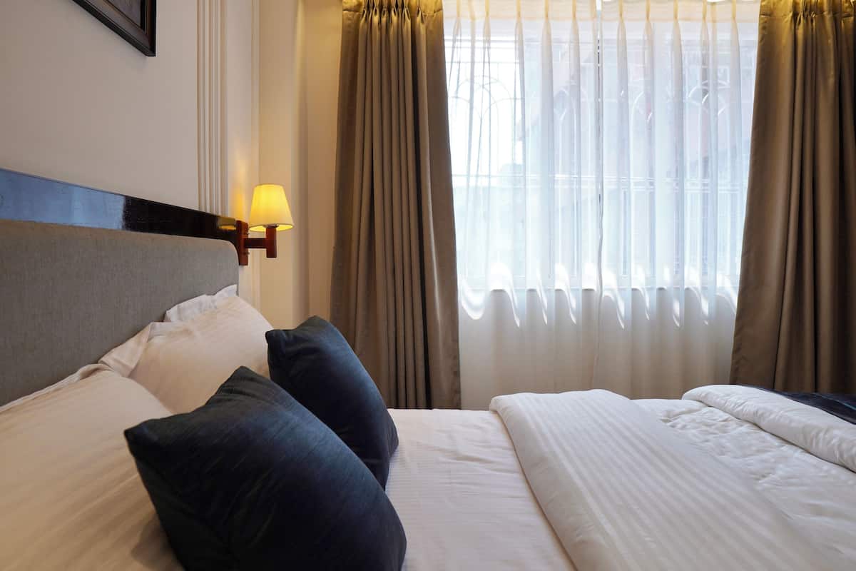 A hotel room with a bed, pillows, a lamp, and curtains.