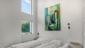 Ett sovrum med en stor säng, ett fönster, en tavla på väggen och en hängande lampa.