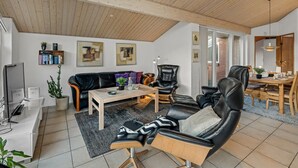 Ett modernt vardagsrum med ett träpanelat tak, en svart lädersoffa, ett soffbord och en matplats med ett träbord och stolar.