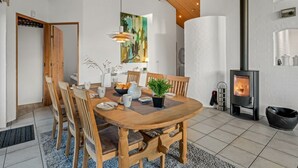Ett modernt matområde med ett träbord och stolar, en tavla på väggen och en vedeldad kamin.