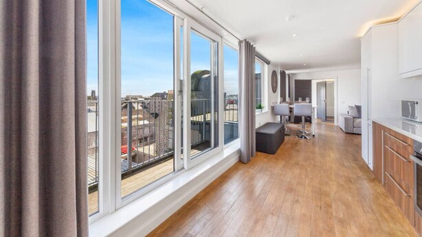 Un appartement spacieux doté de grandes fenêtres, d’une cuisine moderne et d’un balcon.