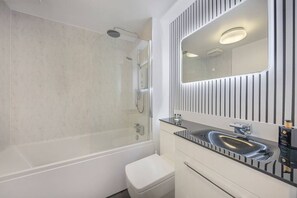 A modern bathroom with a glass-enclosed shower, a white toilet, a vanity with a black countertop, and a mirror with vertical lines.