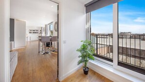 Un appartement moderne avec un plancher en bois, un coin repas doté de tabourets de bar, une plante en pot et une grande fenêtre offrant une vue sur le paysage urbain.