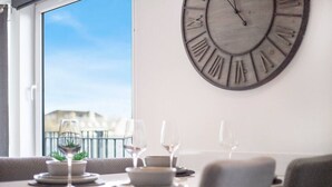 Un coin repas agrémenté d’une grande horloge murale, d’une table dressée pour quatre personnes et d’une vue sur un balcon doté d’une balustrade.