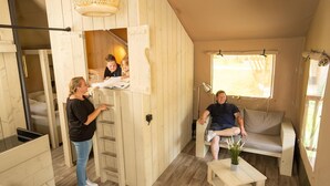 A cozy room with a wooden loft bed, a sofa, and a small table with a plant. - Luxuszelt im Serengeti Park (Hodenhagen)