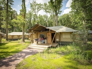 Un camping con una estructura central de madera, una zona de estar cubierta y un camino de ladrillo que conduce hacia ella.