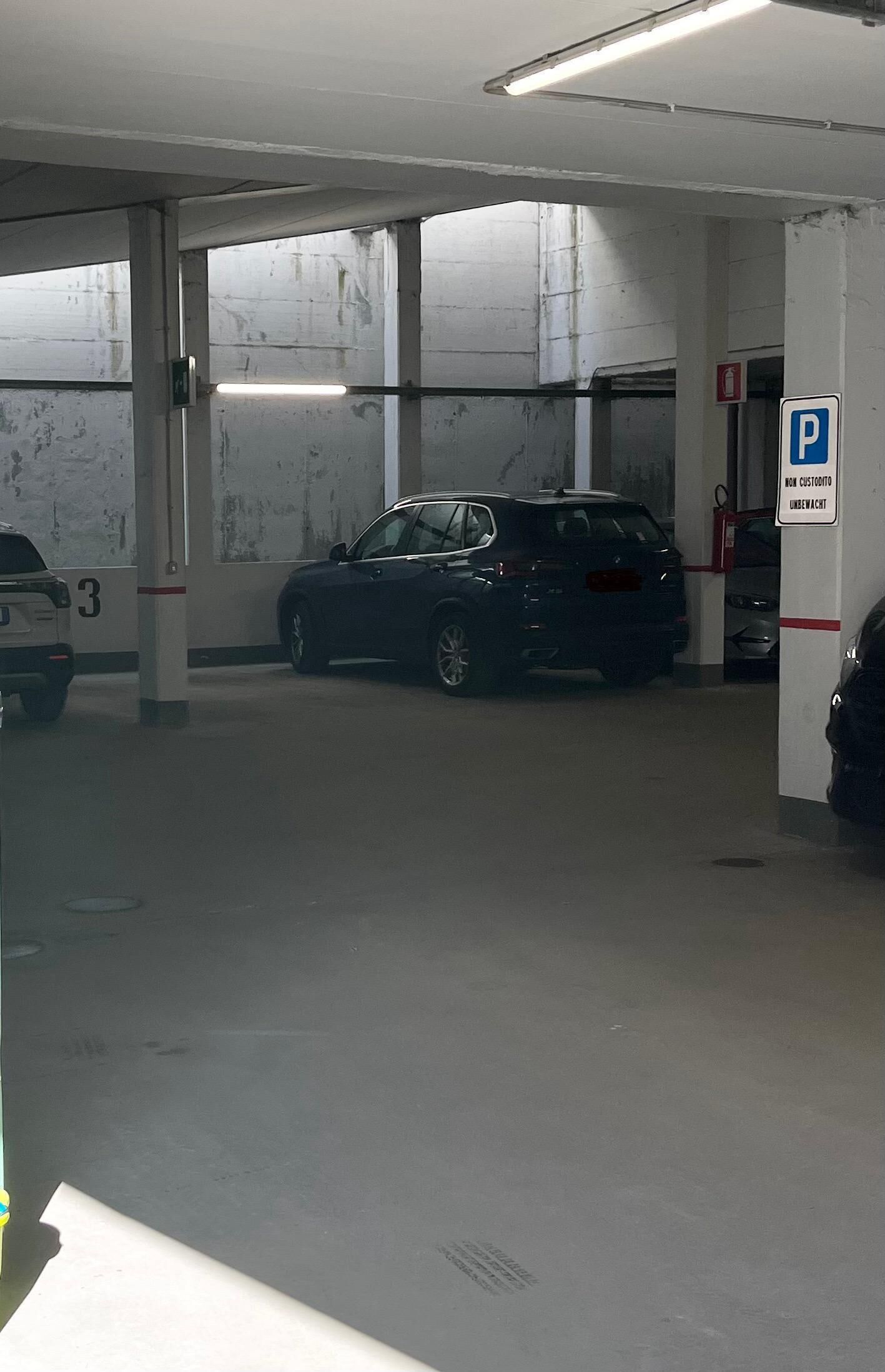 Un parking avec des piliers en béton, un SUV bleu et un panneau indiquant une zone de stationnement.